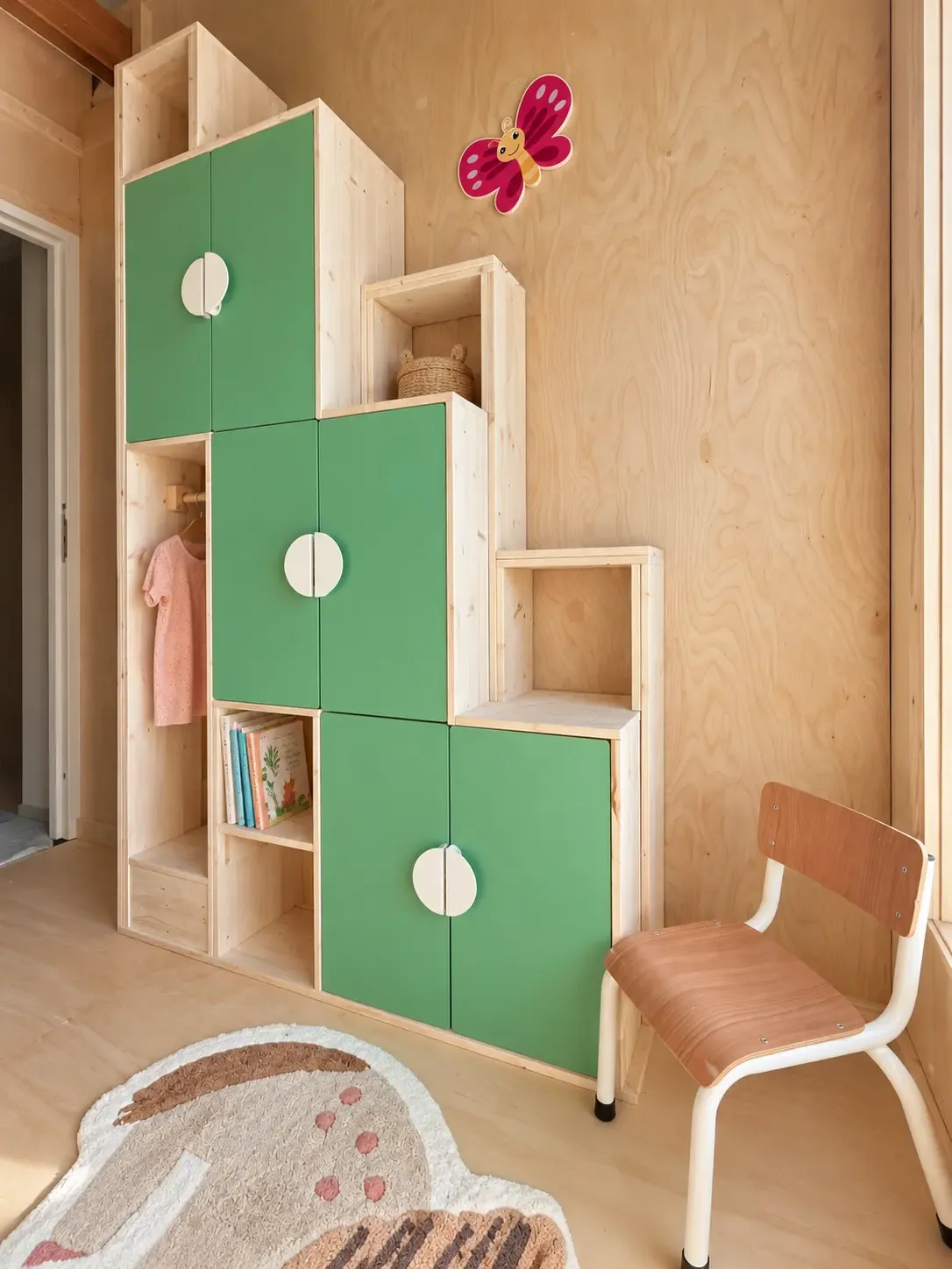 Groene kasttrap met open vakken, kledingroede en een vlinder aan de houten wand